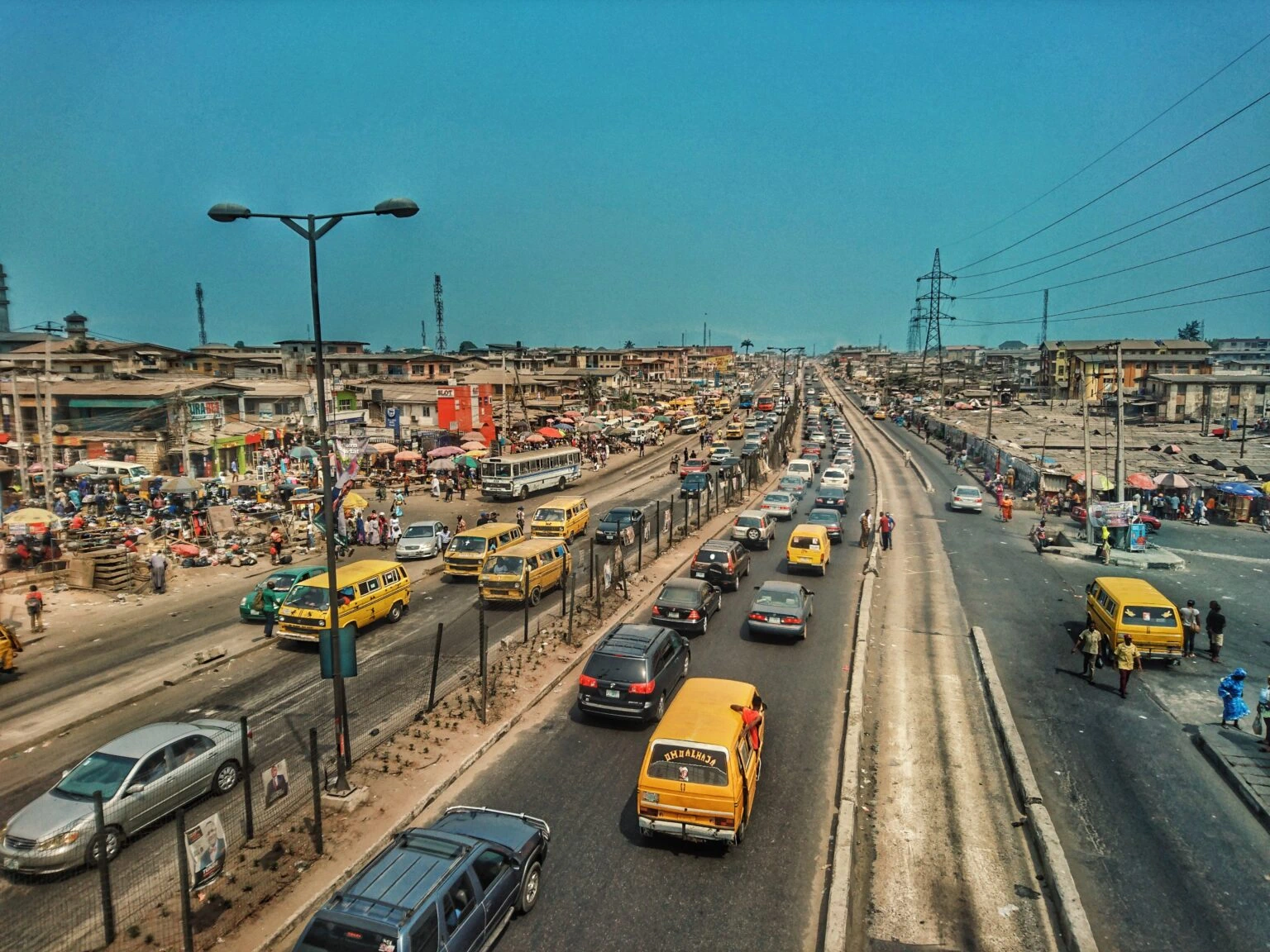 Busy main road in Kosofe, Lagos with yellow buses, traffic and local shops